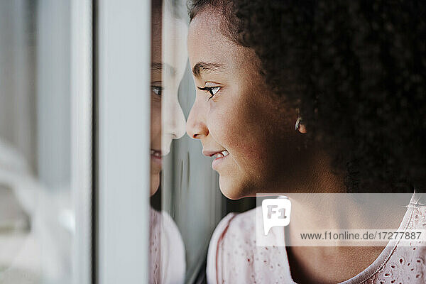 Close-up of cute girl looking through window at home