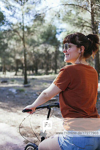 Smiling young woman riding bicycle at countryside during weekend