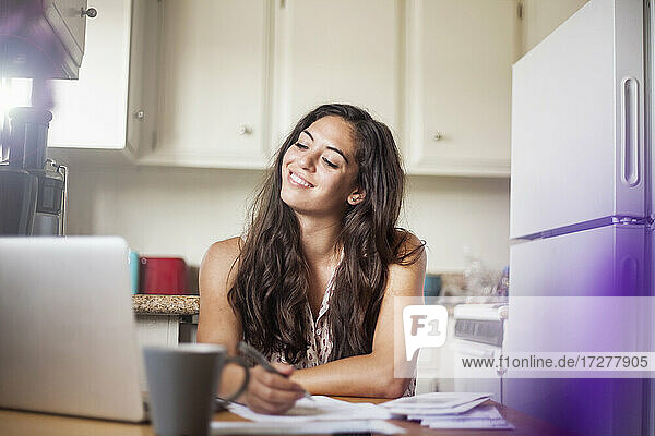 Lächelnde Frau mit Laptop bei der Arbeit in der Küche zu Hause