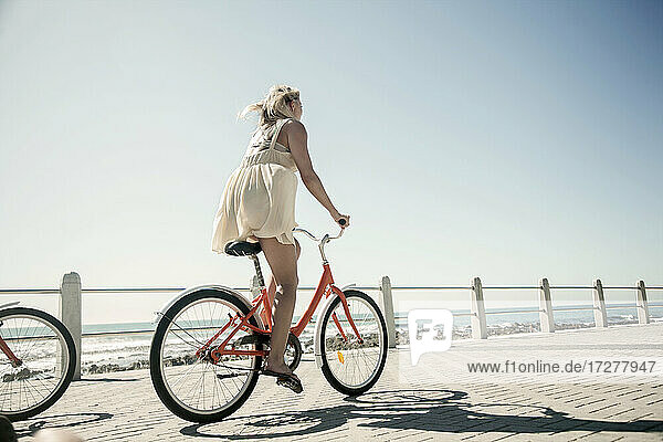 Young woman cycling on promenade against clear sky on sunny day
