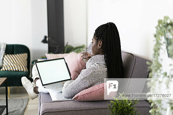 Junge Geschäftsfrau  die Wasser trinkt und am Laptop arbeitet  während sie zu Hause sitzt
