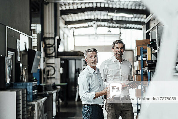 Smiling engineers with digital tablet standing in manufacturing industry