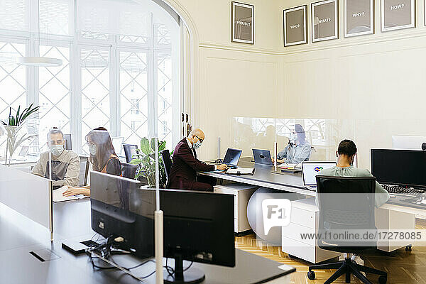 Geschäftsleute mit Schutzmaske bei der Arbeit am Schreibtisch im Büro