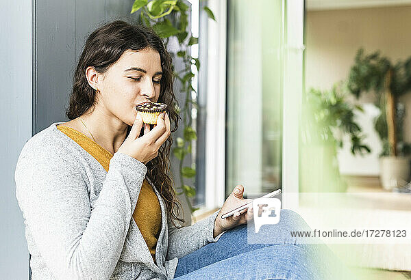 Junge Frau isst Muffin  während sie zu Hause sitzt