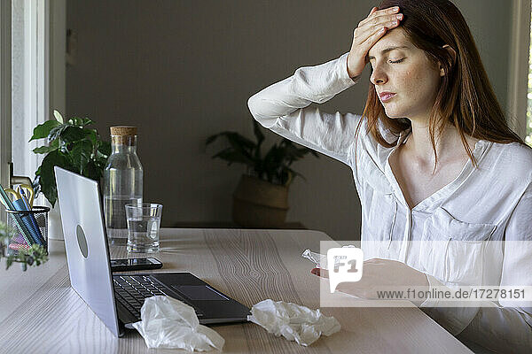 Kranke Frau  die zu Hause am Laptop mit einem Arzt spricht und Kopfschmerzen hat