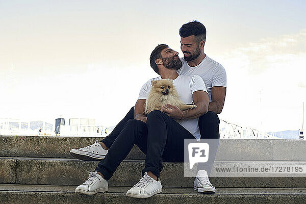 Smiling gay couple with dog sitting on steps against sky