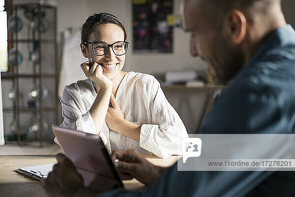 Lächelnde Frau  die einen Mann ansieht  der ein digitales Tablet benutzt  während er im Büro sitzt