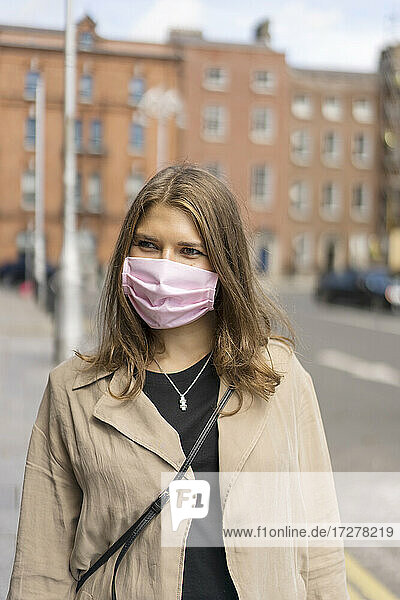 Young woman wearing protective face mask standing on street in city during covid-19