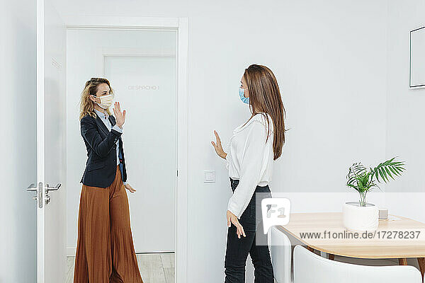 Frau mit Gesichtsmaske winkt mit der Hand an der Tür im Büro