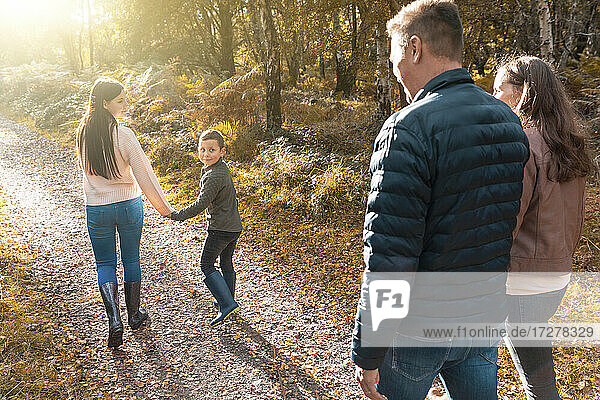 Geschwister schauen über die Schulter auf ihre Eltern  die im Herbst im Park spazieren gehen