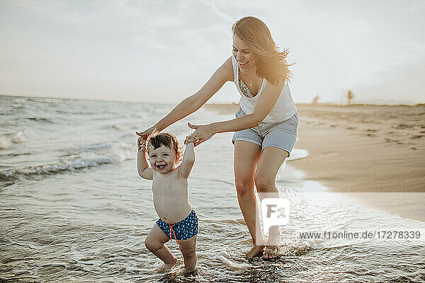 Cheerful mother and son enjoying in water at beach on sunny day during sunset