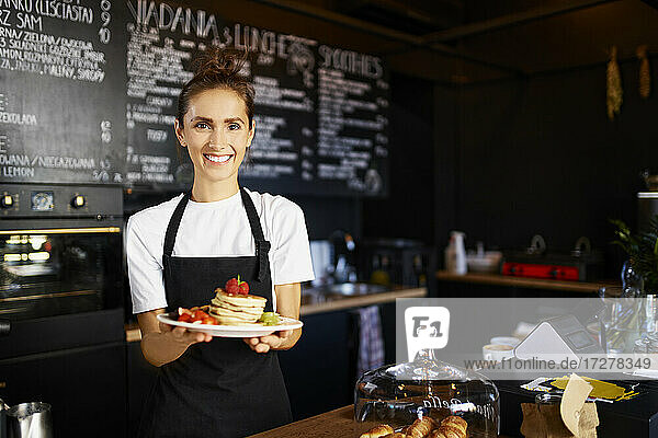 Portrait of smiling female barista giving pancakes in plate at cafe