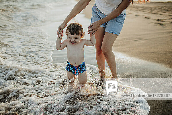Midsection von Mutter mit Sohn genießen im Wasser am Strand an einem sonnigen Tag
