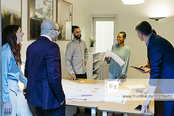 Smiling male and female entrepreneurs discussing over blueprint on table in office
