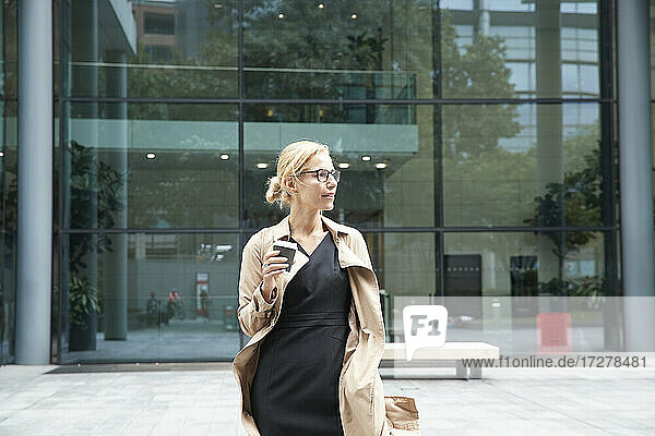 Frau hält Kaffeetasse  während sie vor einem Bürogebäude steht