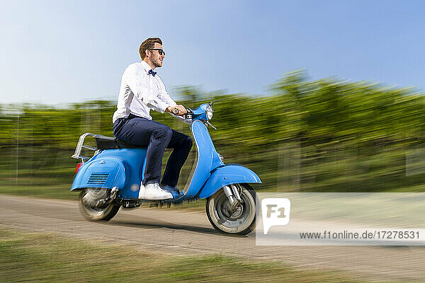 Hübscher junger Mann fährt Motorroller auf der Straße am Weinberg