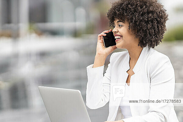 Geschäftsfrau mit Laptop  die im Freien sitzend mit ihrem Mobiltelefon spricht