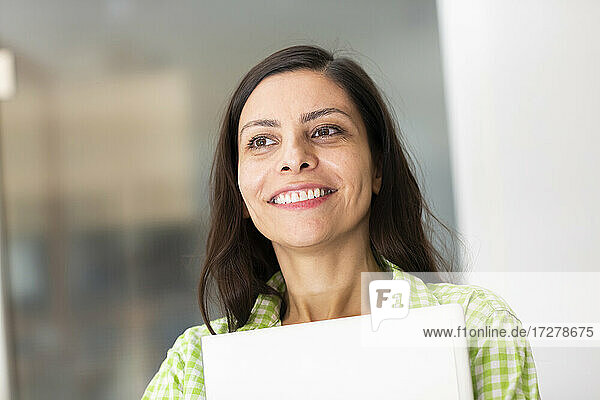 Lächelnde Frau  die einen Laptop hält  während sie zu Hause steht