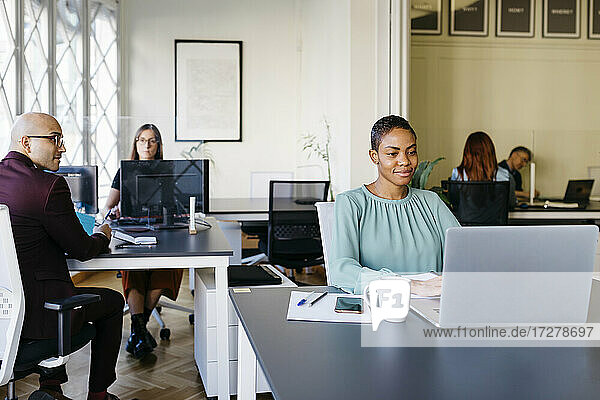 Lächelnde Geschäftsfrau arbeitet am Laptop am Schreibtisch im Büro