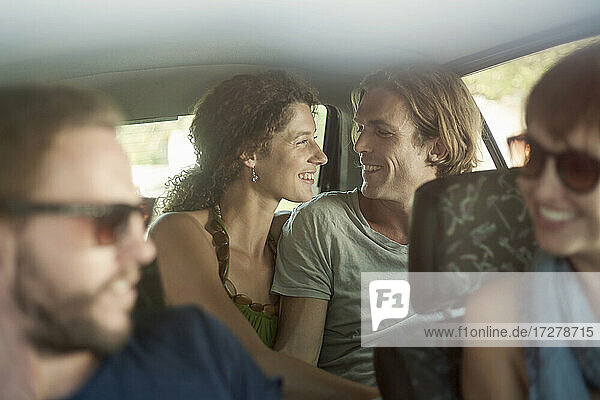 Lächelndes Paar mit Freunden im Auto sitzend während einer Autoreise