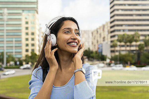 Fröhliche junge Geschäftsfrau  die über Kopfhörer Musik hört  gegen die Stadt