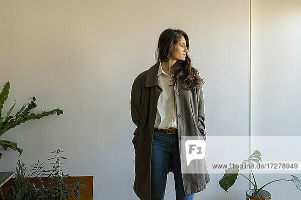Female model with hands in pockets looking away while standing at home
