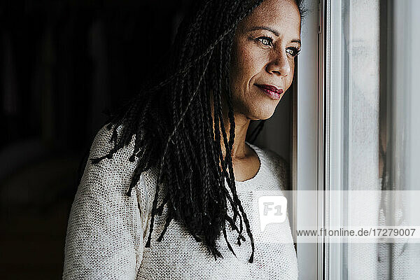 Nachdenkliche Frau  die durch ein Fenster schaut  während sie zu Hause steht