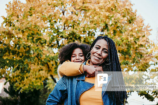 Smiling mother piggybacking daughter while standing at park