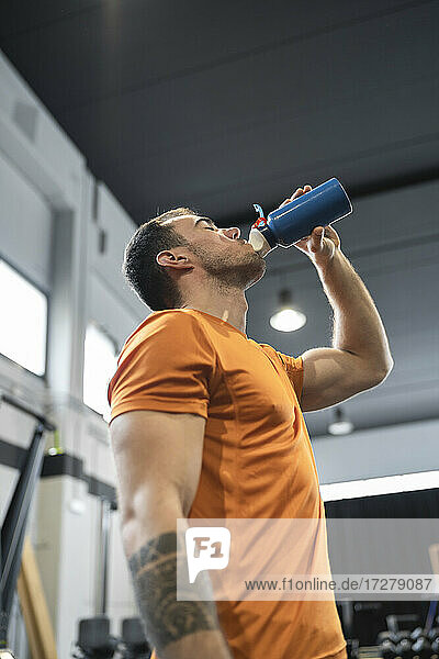 Durstiger Mann trinkt Wasser  während er in einer Turnhalle steht