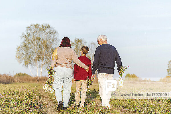 Älteres Ehepaar geht mit Enkel auf einem Feld spazieren