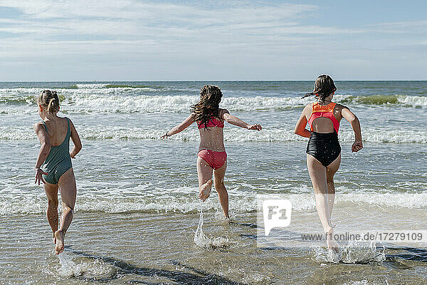 Friends running in water at beach on sunny day