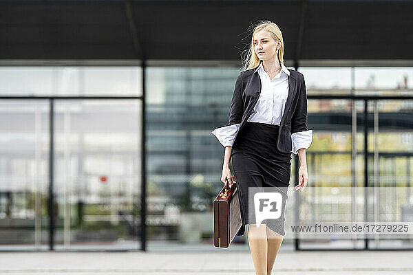 Blond businesswoman walking with briefcase against building
