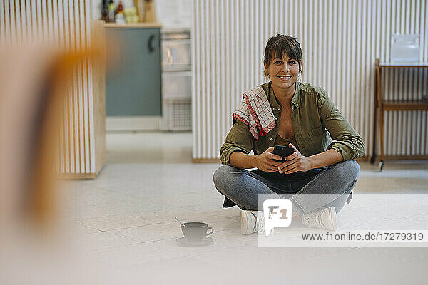 Lächelnde Geschäftsfrau  die ein Smartphone benutzt  während sie in einem Café auf dem Boden sitzt