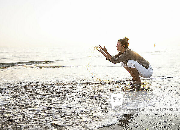 Schöne junge Frau  die am Strand bei Sonnenuntergang im Wasser plantscht
