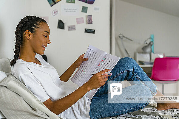 Teenager-Mädchen liest in einem Schulheft  das zu Hause auf dem Bett liegt