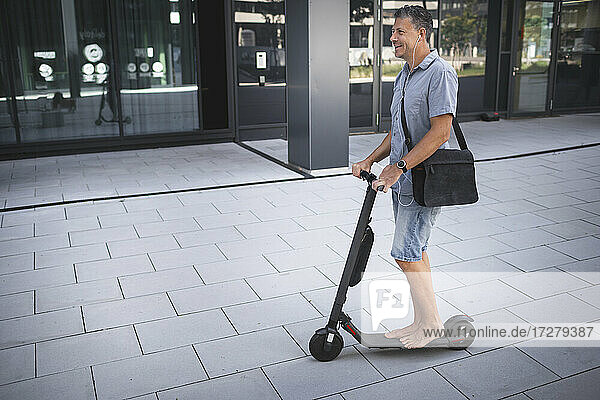 Mature man listening music while standing on electric push scooter