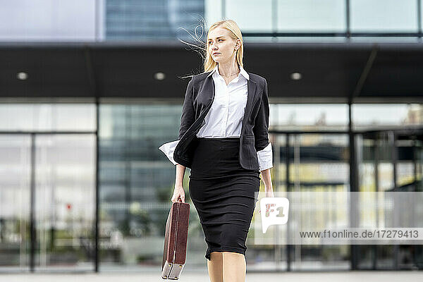 Businesswoman holding briefcase while walking against building
