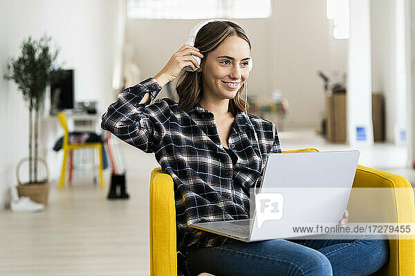 Smiling woman wearing headphones while working on laptop at home