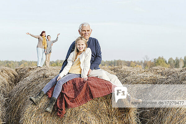 Großvater und Enkelin sitzen auf einem Heuballen  Großmutter und Enkel im Hintergrund
