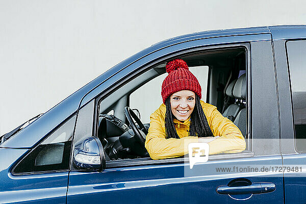 Lächelnde Frau mit verschränkten Armen  die während einer Autoreise durch das Autofenster schaut