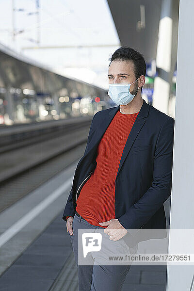 Male entrepreneur wearing protective mask while looking away on railroad station platform