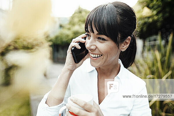 Lächelnder weiblicher Ingenieur  der eine Kaffeetasse hält  während er mit einem Mobiltelefon spricht