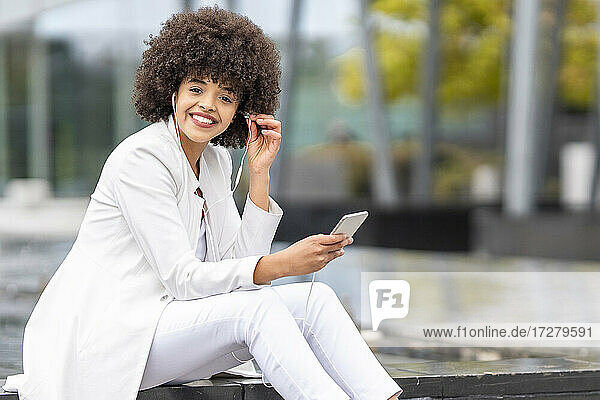 Lächelnde Geschäftsfrau  die Musik hört  während sie ihr Mobiltelefon im Freien benutzt