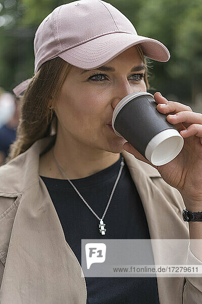 Schöne junge Frau schaut weg  während sie auf der Straße stehend Kaffee trinkt