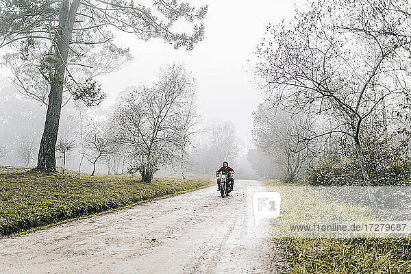 Man riding motorcycle on dirt road in foggy weather