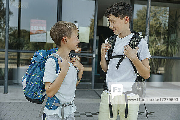 Brüder schauen sich an  während sie vor dem Schulgebäude stehen