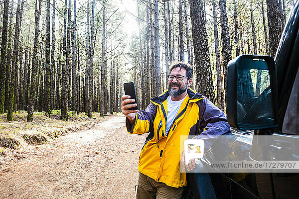 Lächelnder Mann  der ein Mobiltelefon benutzt  während er neben einem Auto im Nationalpark El Teide steht  Teneriffa  Spanien