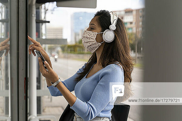 Woman in face mask wearing headphones while purchasing bus ticket during COVID-19