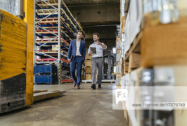 Man using digital tablet while inspecting warehouse with businessman at factory