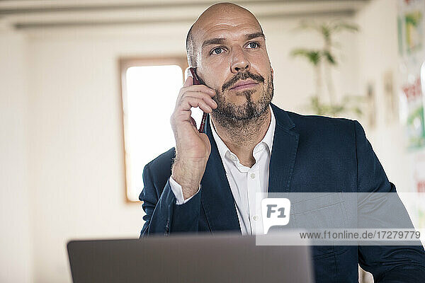 Geschäftsmann  der mit seinem Handy telefoniert  während er im Büro am Laptop arbeitet